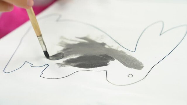 A little girl draws a rabbit with gray acrylic paints, draws on a white T-shirt. The child's work on the fabric. Crafts, preparation for the religious holiday Easter. High quality 4k footage
