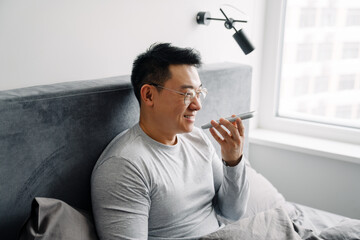 Asian man talking on mobile phone after sleep while sitting in bed