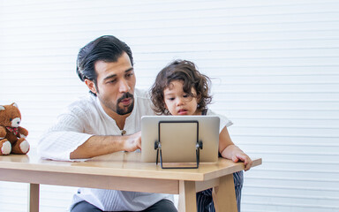 Obraz premium Caucasian handsome father and adorable little daughter playing together and online chatting in tablet while staying in living room at home. Family, Kid, Education and Technology Concept.