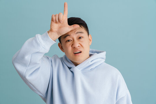 Brunette adult asian man gesturing looser sign at forehead