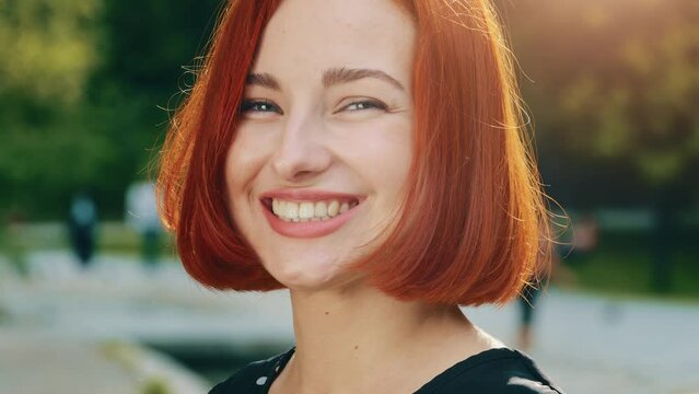 Close up human female face redhead woman girlfriend with natural makeup perfect clean skin smiling toothy smile beautiful attractive model girl lady flirting posing in city park sun shine background