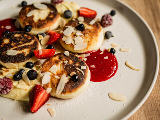  Cheesecakes with English cream, cherry sauce, strawberries, blueberries, currants and almond flakes on a handmade plate