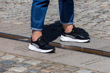 Pair of feet with black sneakers standing on both sides of meridian line on ground at Greenwich observatory.