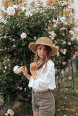 cute little girl with a straw hat for a bush of white roses