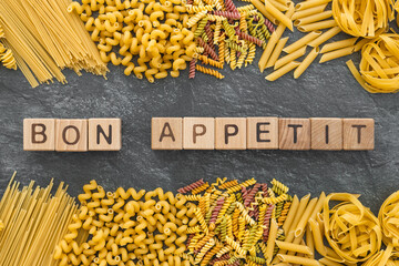 Various pasta and word bon appetit written wooden cubes on dark stone background