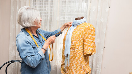 elderly woman measuring an orange dress on a mannequin