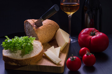 Table-top still life with bread, herbs, tomatoes, cheese, glass of wine and dark bottle