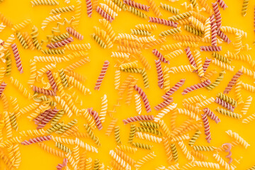 Beautiful Italian uncooked colored farfalle pasta close-up on yellow background. horizontal top view