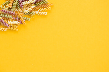 Beautiful Italian uncooked colored farfalle pasta close-up on yellow background. horizontal top view