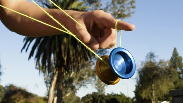 Close Up of a Spinning Yoyo Trick on a Blue and Orange Metal Yoyo with Palm Trees and a Blue Sky in the Background