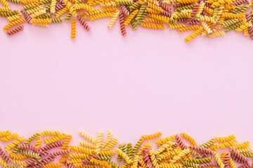 Beautiful Italian uncooked colored farfalle pasta close-up on pink background. horizontal top view