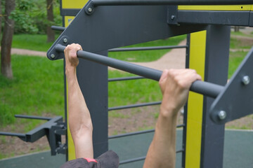 man's hands on the horizontal bar while pulling up in the park in outdoor training