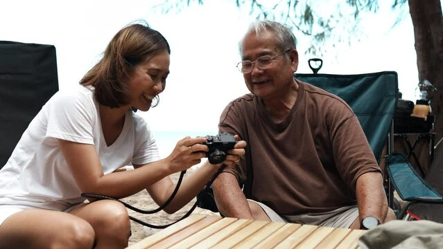 Happy family elderly senior father and daugther looking picture in camera taking memories outside on the beach camping together fun and enjoy life.