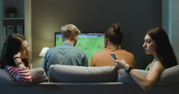 Bored girls talking together while boyfriends are watching soccer