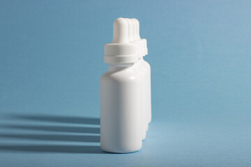 A set of white cosmetic bottles with a dropper lined up with hard shadows. The concept of face and body care at home and in a beauty salon