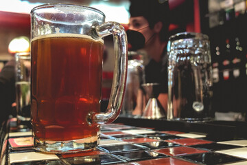 Closeup of big beer mug glass and young latin bartender in the bar from a pub in the night