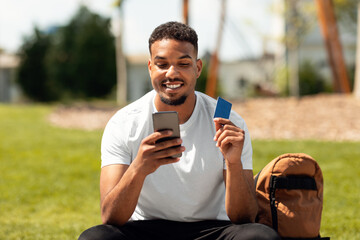 Promo code for purchase or online shopping. Happy black man using smartphone and credit card,...
