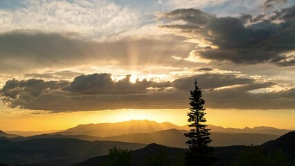 Beautiful sunset time-lapse as sun lights up the clouds with single tree silhouetted against the sky in Utah.