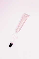 A pink tube with cosmetics and a squeezed creamy cosmetic product on a pink background. Face cream, foundation.