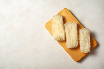 skeins of raw Korean starch noodles tanmen lie next to each other on a wooden board on a gray background, copy space.