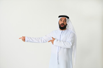 Arab Emirati man pointing to side looking happy and surprised. Arabian UAE Muslim businessman excited for new offer isolated on white background