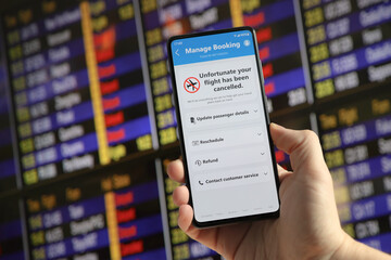 Flight cancelled. Man holding mobile phone in airport terminal. Smartphone application announces bad news to tourist. Strike or problem with plane.  Timetable and schedule in the blurred background.