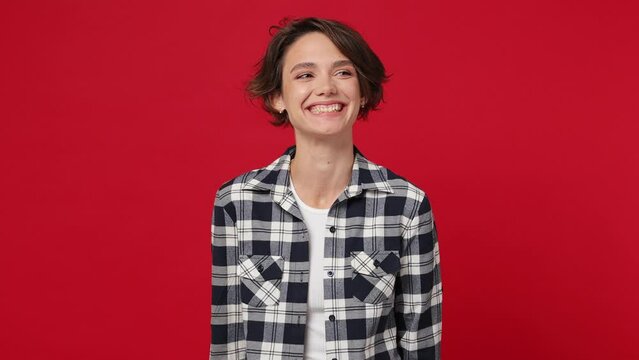 Smiling happy young woman 20s she wearing basic white t-shirt checkered shirt look around think dream lost in thought and conjectures isolated against over plain solid dark red color wall background