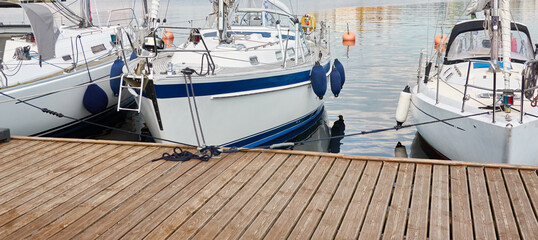 White modern sailboat (for rent and sale) moored to a pier in a yacht marina. Wooden teak deck....