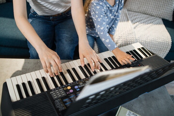 Close up of hands and piano keys. Little girl child learning to play classic digital piano with her young mom at home. Small kid preschool student playing musical instrument with mother.