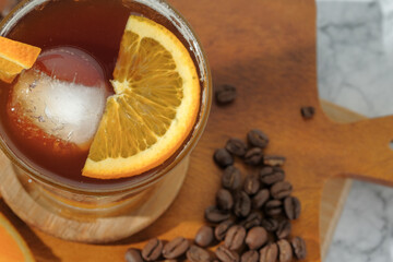 cold Iced black coffee mixed with orange juice and orange slices in glass on wooden plate in white background with nature leaves silhouette shadow. two tones layer fresh summer drink in the morning