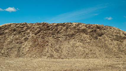 a product of wood processing, in the photo mountains of wood chips and sawdust against a blue sky