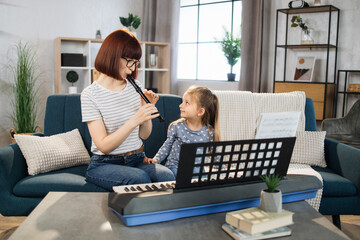 Mom and little happy girl in music therapy by playing flute on music room. Teacher helping young female pupil in flute lesson. Relaxing at home. © sofiko14
