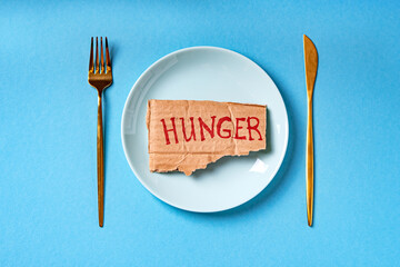 Text Hunger written on a cardboard lying on the empty plate. Food crisis, global hunger, food supply issue concept.