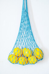 Zero waste mesh bag filled with lemons hangs on the white wall. Vertical photography.