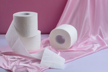Three rolls of white perforated toilet paper, one unwound, on a pink silk background