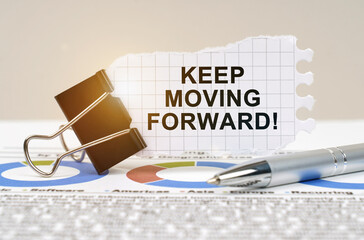 On the table are reporting charts, a pen, in a clip paper with the inscription - KEEP MOVING FORWARD