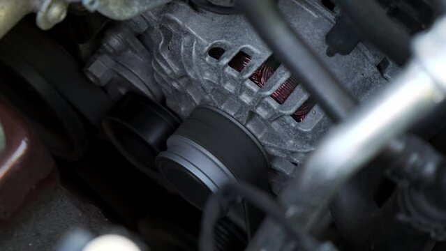 Close up spinning car generator under car hood. working machine stands still and there are moving parts inside it. You can see alternator belt, which transmits torque to air conditioning compressor.
