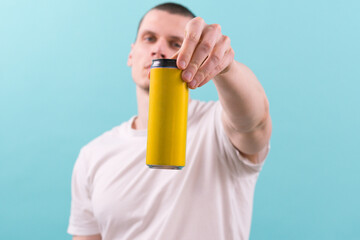 A man in a white t-shirt holds a yellow empty aluminum can on a blue background. Metallic. Mock....