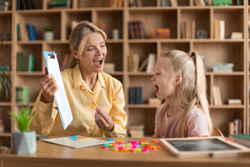 Cheerful female speech therapist curing child's problems and impediments, little girl learning letters during lesson