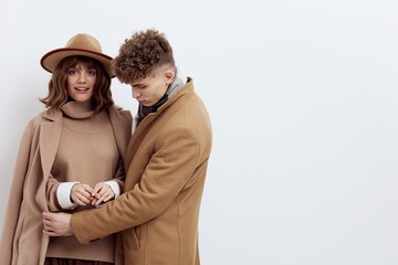 a beautiful couple in love is standing on a white background in autumn clothes and a man is carefully buttoning a coat on a woman
