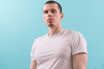 A confident man in a white t-shirt looks on the sideway on a blue background. Modern. Studio. White. Young. Casual. Fashion. Lifestyle. Authority. Concentration. Hold