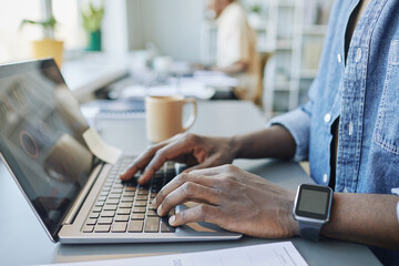 Side view close up of African American man working in office with focus on hands typing at laptop keyboard, copy space