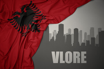 abstract silhouette of the city with text Vlore near waving national flag of albania on a gray background.