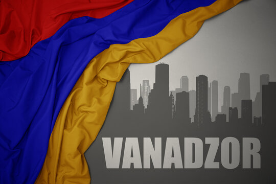 abstract silhouette of the city with text Vanadzor near waving national flag of armenia on a gray background.