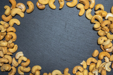 Round frame of cashew nuts top view on black slate board.