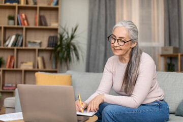 Concentrated european mature lady teacher with gray hair in glasses works with computer, have meeting remotely