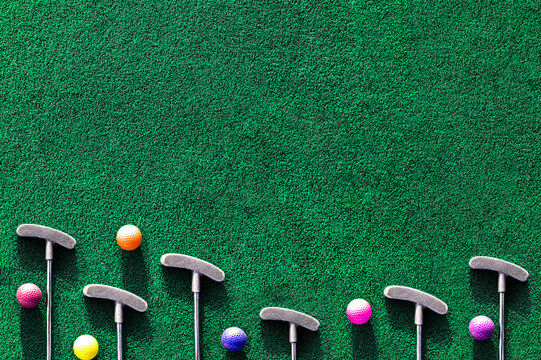 Multiple mini golf clubs and balls on putting green background with copy space