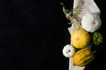 Decorative pumpkins white, yellow, green lie on a linen napkin and on a black background