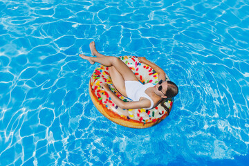 A slender woman in a white swimsuit and sunglasses lies in the pool on an inflatable circle. Summer rest.