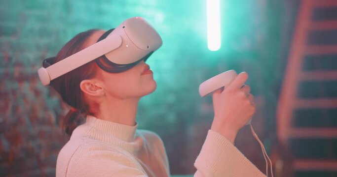 Young woman wearing vr goggles and using handles to experience the metaverse